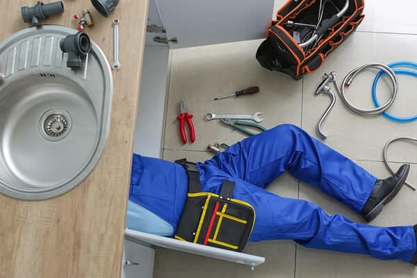 A plumber, lying under a kitchen sink, makes repairs with a variety of plumbing tools