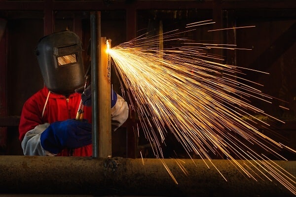A welder wears protective head gear while creating sparks with a torch