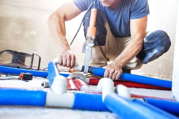 A tradesman uses tools important to the history of pipefitting to assemble blue and white pipes