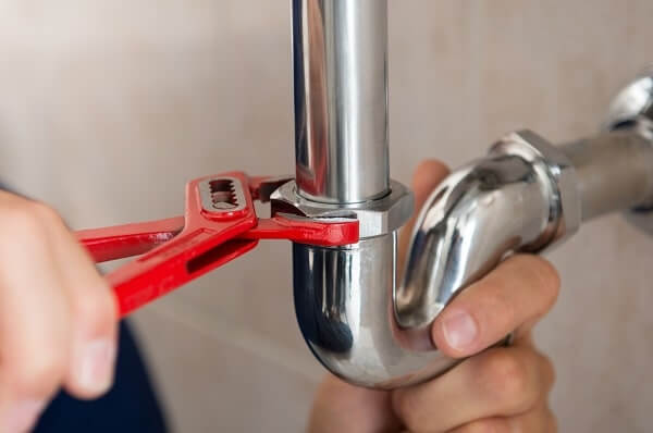 A plumber uses a red wrench to install a pipe under a sink