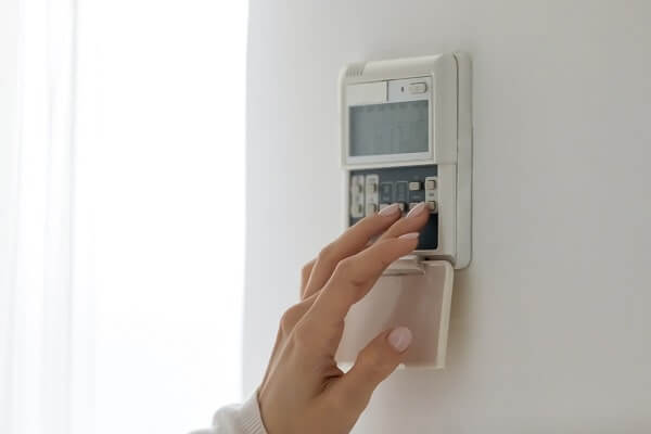 A woman's hand presses buttons on a smart thermostat in her home