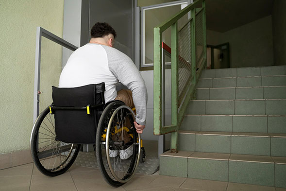 A man uses a wheelchair to cross a ramp and enter his home