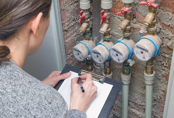 A plumber with a clipboard checks water meters to ensure compliance with plumbing regulations