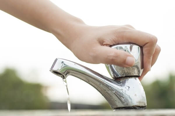 A person's left hand turns off a leaking faucet to conserve water