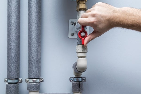 A plumber’s hand turns a backflow valve to adhere to building safety codes