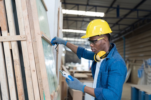 A construction worker wears a yellow hard hat while inspecting wood slabs