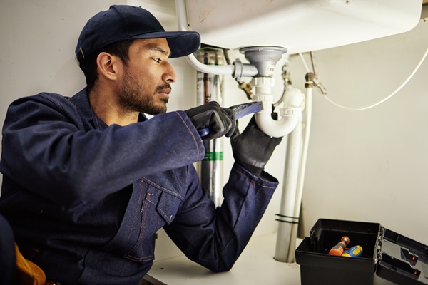 A plumber tightens a pipe under a sink