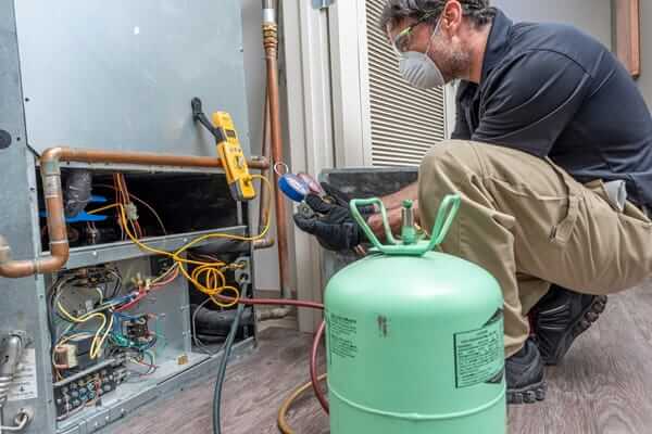 A technician wears a mask and PPE to perform maintenance on refrigeration systems