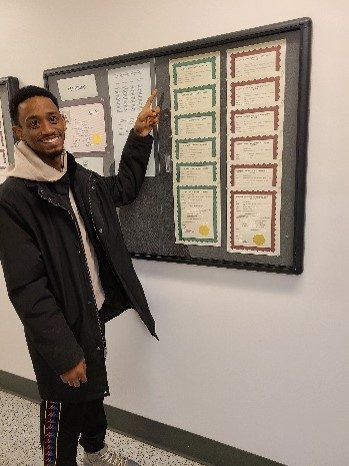 Julio Hernandez, Apex graduate, smiles and points at his Plumbing & Pipefitting certification